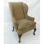 A Georgian style wing armchair, raised on short cabriole legs with carved knees and knurled feet,