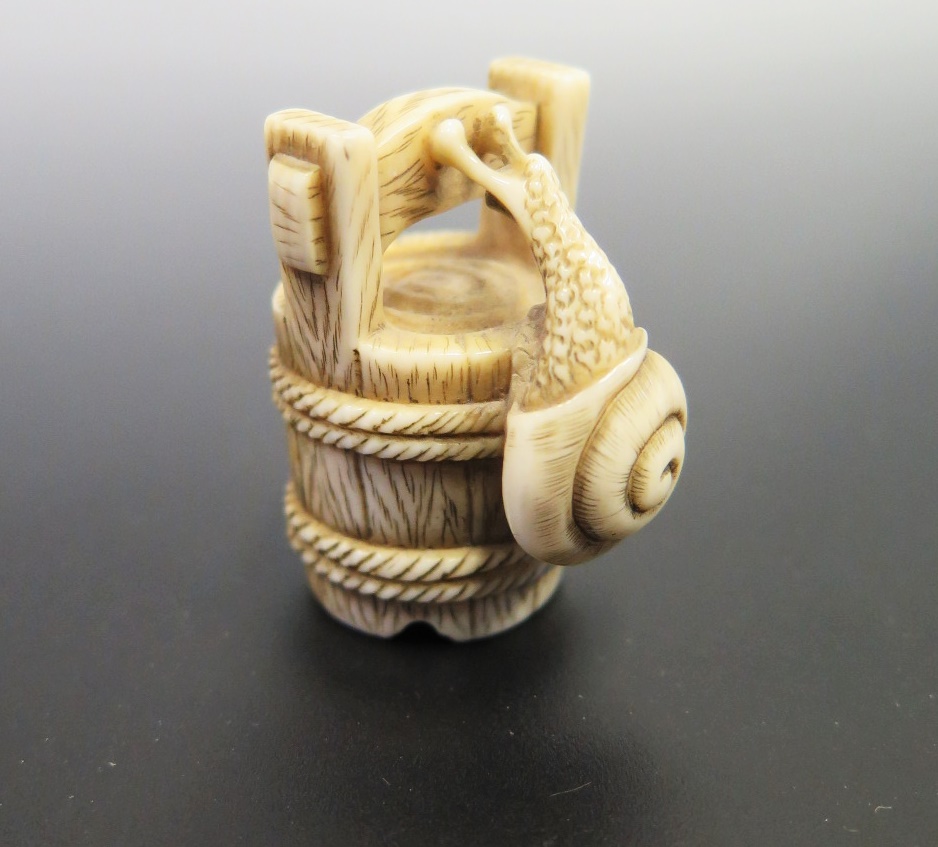 A Japanese Ivory Netsuke carved in the form of a snail climbing a bucket, signed to the base, c.