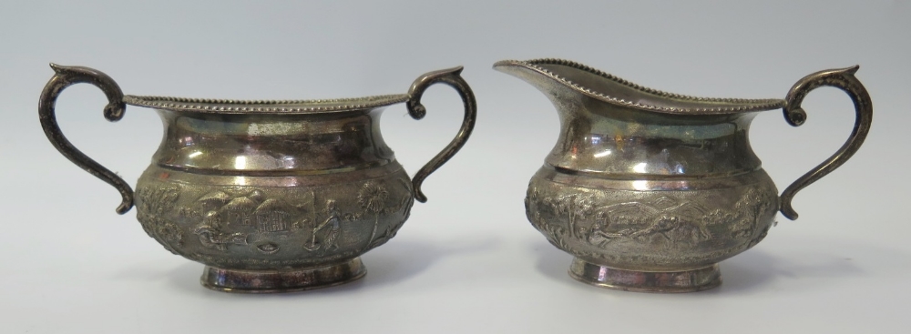 An Indian Silver Sugar and Creamer decorated with continuous landscape scene with figures and