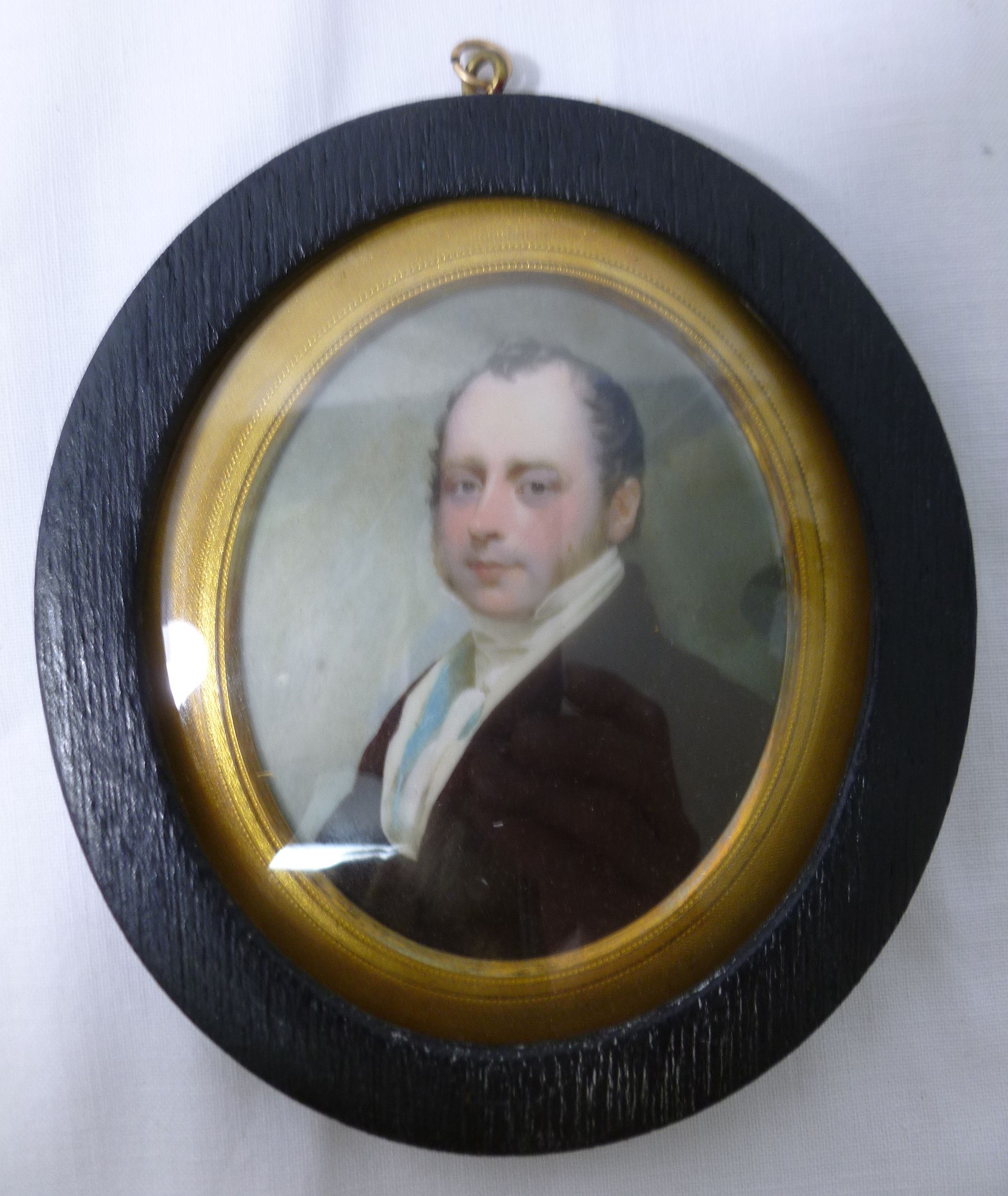 A 19th century oval portrait miniature of a gentleman, wearing a black coat,