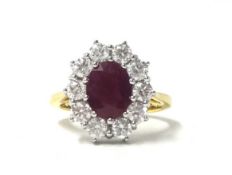 An 18ct gold ruby and diamond cluster ring, claw set with an oval mixed cut stone bordered by ten
