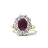 An 18ct gold ruby and diamond cluster ring, claw set with an oval mixed cut stone bordered by ten