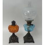 Two traditional oil lamps with coloured glass reservoirs.