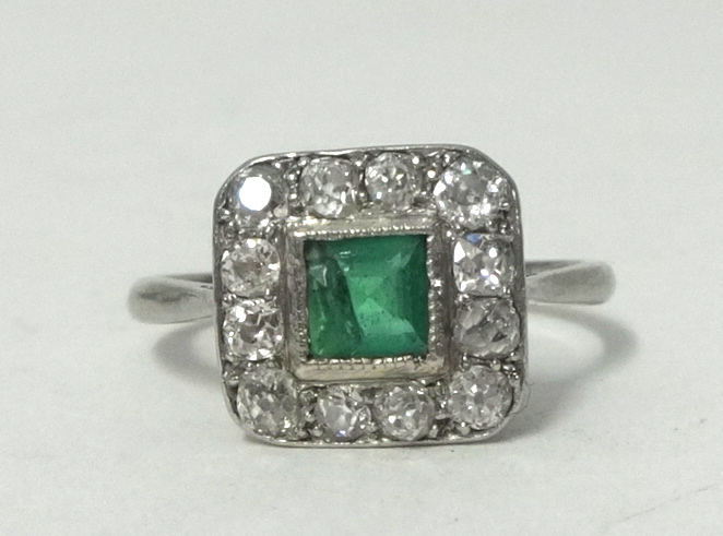 A platinum, emerald and diamond set square ring, size N.large chip to stone