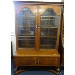 An oak bookcase with two arch glazed doors on a cupboard base.