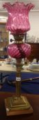 An oil lamp with cranberry glass shade and reservoir, on a brass Corinthian column base