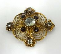 A antique yellow metal brooch set with garnets and of scrollwork design.