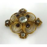 A antique yellow metal brooch set with garnets and of scrollwork design.