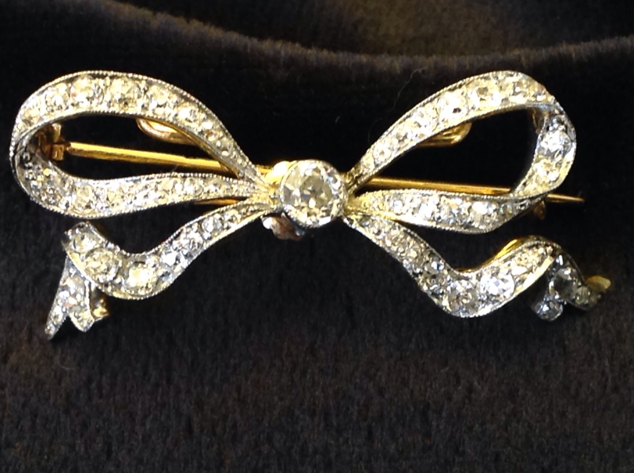 An 18ct gold diamond bow brooch, the ribbon bands set with diamonds around a central brilliant cut