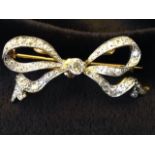 An 18ct gold diamond bow brooch, the ribbon bands set with diamonds around a central brilliant cut