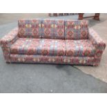 A three-seater tapestry style upholstered sofa, having loose cushions, raised on casters.