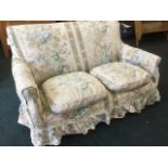 A small sprung upholstered sofa, with floral linen loose covers and down cushions, raised on