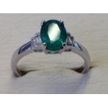 A hallmarked 18ct white gold oval emerald & diamond ring, the main claw set stone of over three-