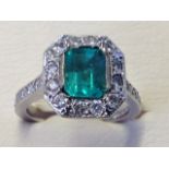 An 18ct gold emerald cut Columbian emerald & diamond cluster ring, the bezel set emerald of over one