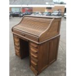 An Edwardian oak roll-top desk having shaped tambour enclosing a fitted interior with pigeonholes