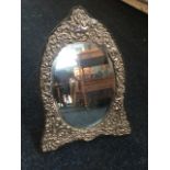 A hallmarked silver dressing table mirror, the oval bevelled plate in scroll embossed frame -