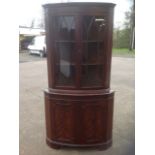 A reproduction bowfronted mahogany corner cabinet, with dentil cornice above astragal glazed