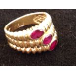 An 18ct gold ruby three stone ring, the oval offset bezel mounted stones in three snake-like