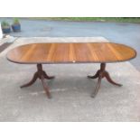 A Georgian style mahogany dining table, the crossbanded top supported on twin turned pedestals, with