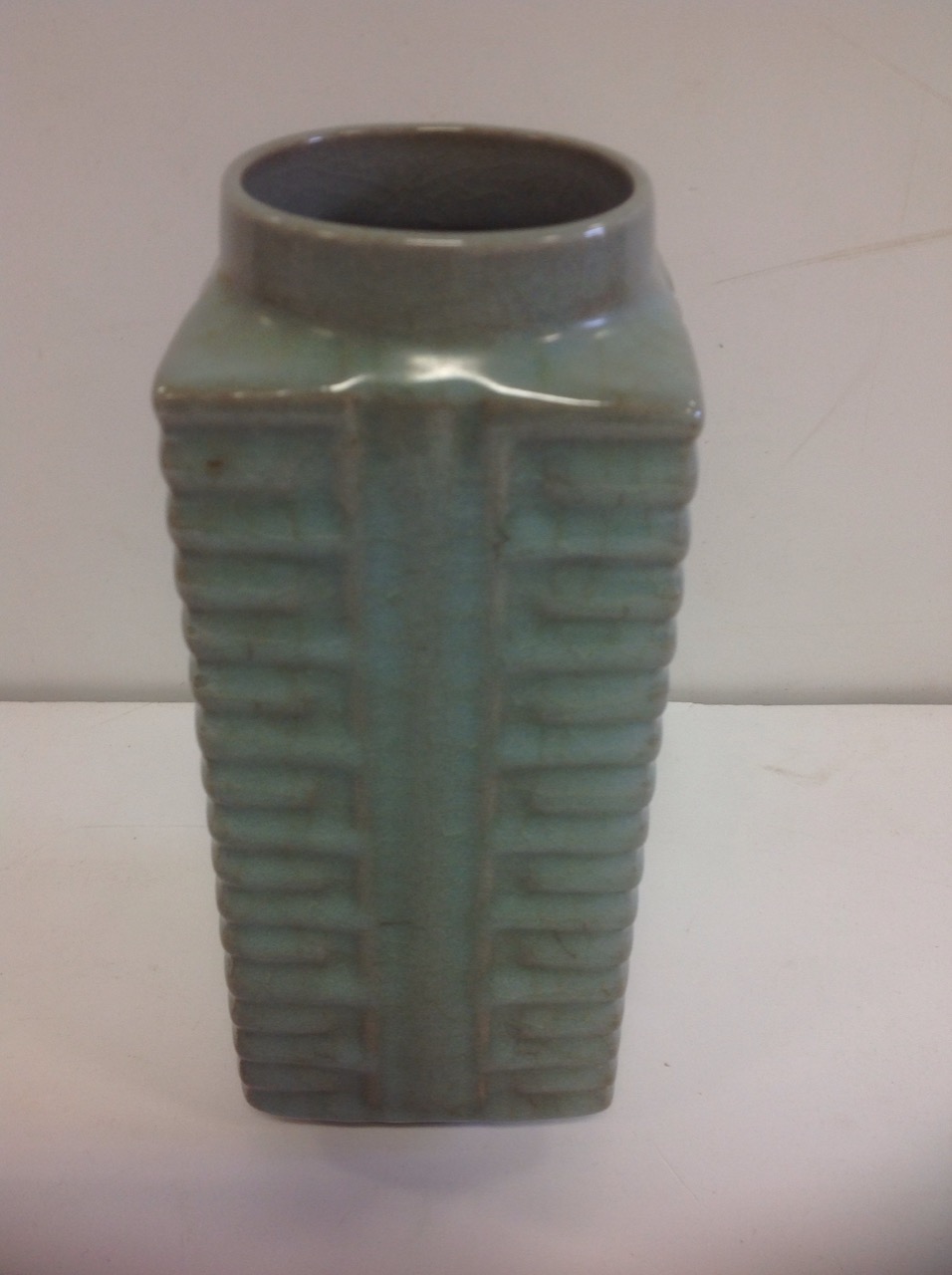 A square Chinese stoneware celadon glazed vase, with circular rim above a ribbed body, decorated