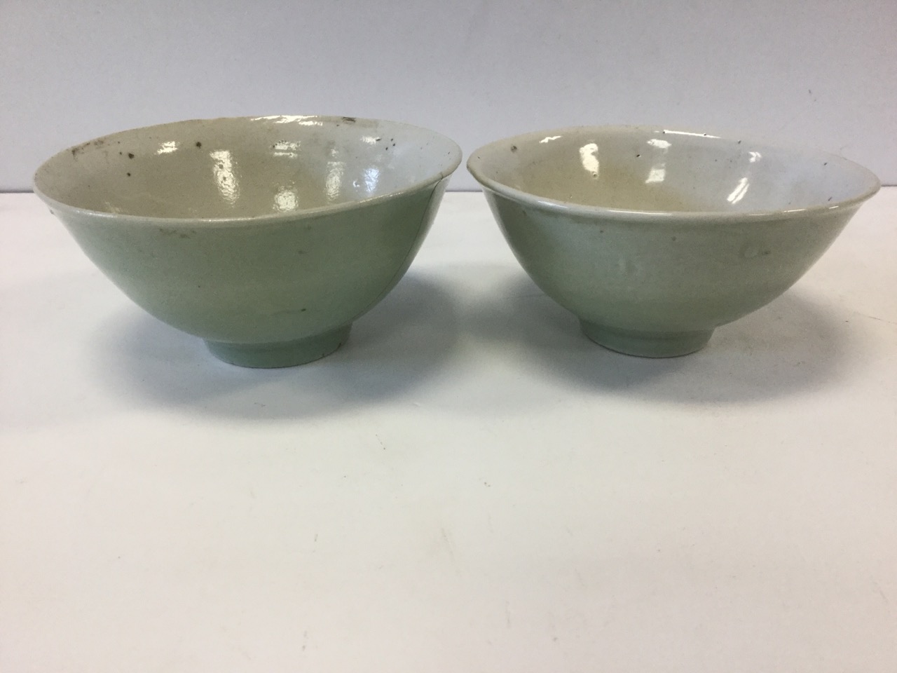 A pair of early Chinese celadon glazed bowls, raised on tubular bases, unmarked and one