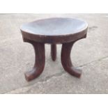 A tribal art adzed carved stool, the circular dished bowl seat on shaped legs, carved out of the