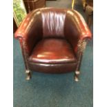 A red leather upholstered tub armchair, with brass studding and bowfronted seat, raised on stub