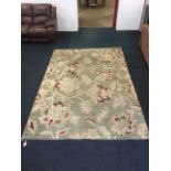 A large modern floral rectangular rug woven with leaves & flowers on pale green ground. (117in x