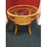 A circular cane dining table, having plate glass top above a cross-trellis apron with shelf below,