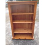 A reproduction pine open bookcase, with shaped top above an arched apron, the adjustable shelves