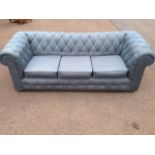 A chesterfield sofa, having button upholstery with three loose cushions, raised on casters.
