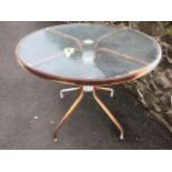 A circular glass topped garden table on tubular metal frame.