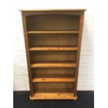 A pine open bookcase, with arched apron above adjustable shelves framed by fluted stiles, raised