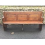 A 6.5ft pine pew with panelled back and solid seat, the shaped ends numbered with painted shields.