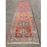 An oriental runner woven with hooked and serrated medallions on madder ground, the frieze of