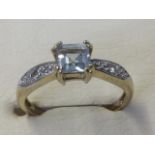 A 9ct yellow gold aquamarine & diamond ring, the emerald cut pale aquamarine claw set above