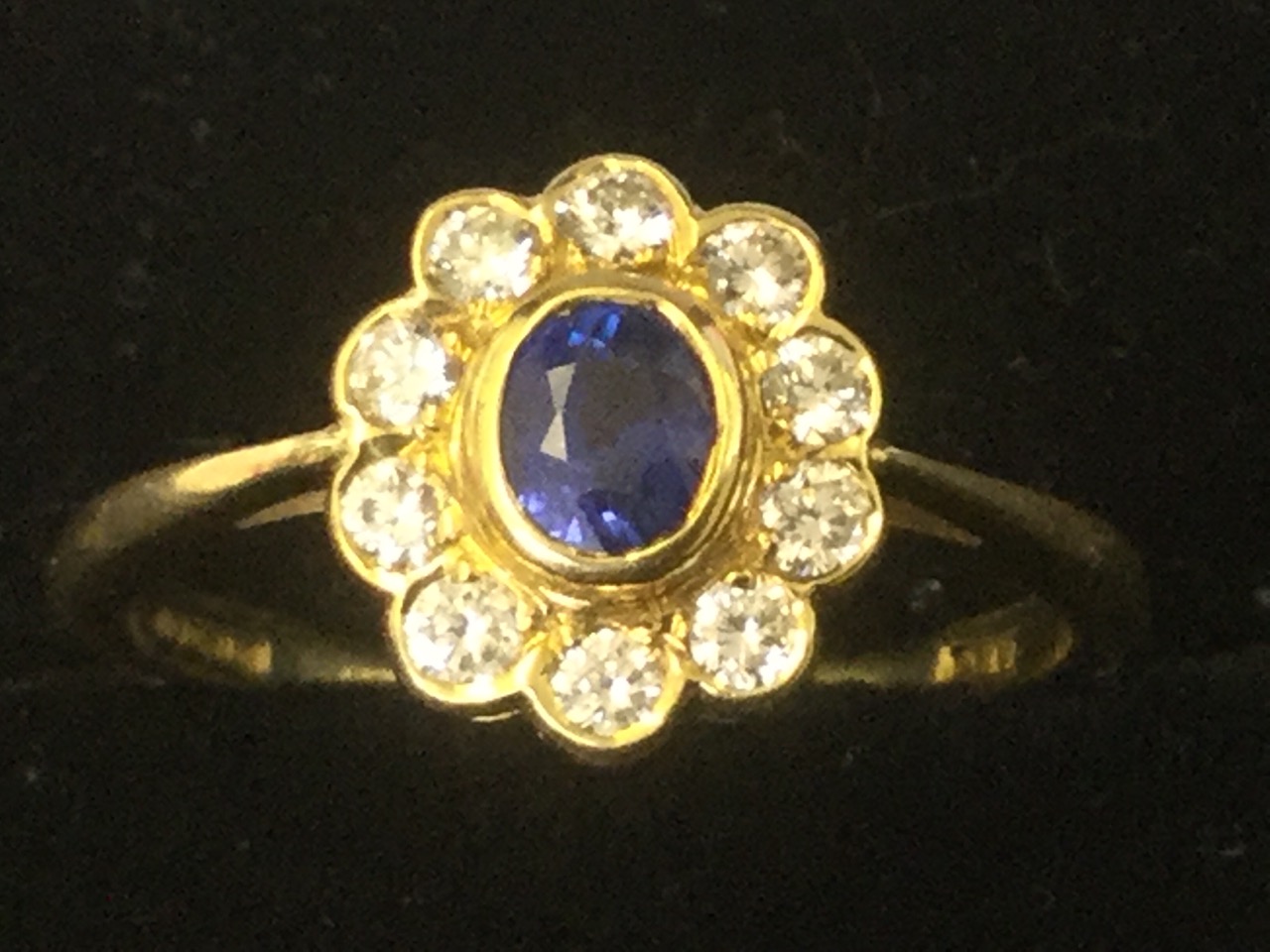 A 18ct yellow gold sapphire & diamond cluster ring, the oval bezel set sapphire framed by a border