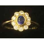 A 18ct yellow gold sapphire & diamond cluster ring, the oval bezel set sapphire framed by a border