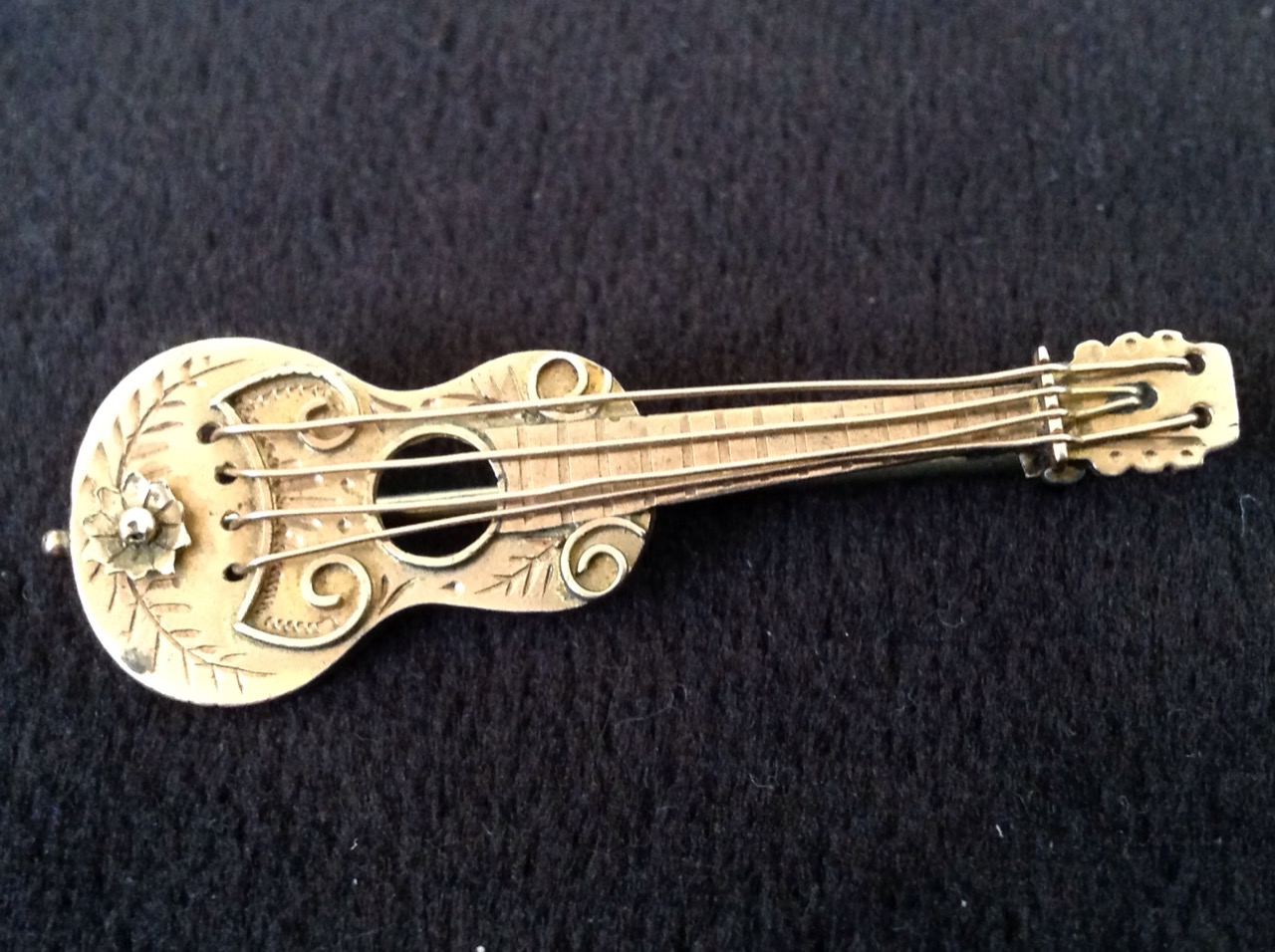 A 9ct gold guitar brooch decorated with scrolling and a flowerhead, mounted with hinged pin to verso