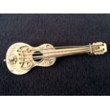 A 9ct gold guitar brooch decorated with scrolling and a flowerhead, mounted with hinged pin to verso