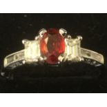 An 18ct fancy sapphire and diamond ring, the oval claw set red sapphire bordered by emerald cut