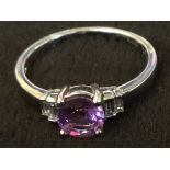 An 18ct gold purple sapphire & diamond ring, the circular sapphire of 0.80 carats, above shoulders