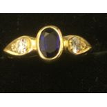 An 18ct gold sapphire & diamond three stone ring, the bezel set oval sapphire flanked by teardrop