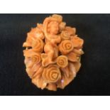 An oval carved coral brooch with cenral cherub framed by flowers and leaves, the panel mounted on