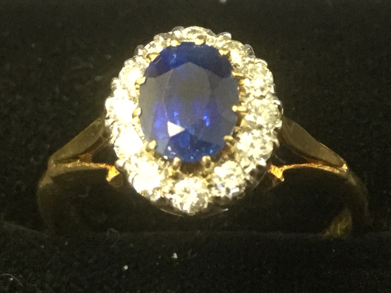 A sapphire & diamond ring, the oval claw set sapphire of over a carat, framed by twelve diamonds