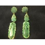 A pair of jade drop earrings, the flowerhead studs with scrolled keepers supported oval carved