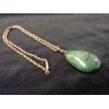 A pear shaped carved jade pendant with 9ct gold mount, fitted on an unmarked yellow metal link