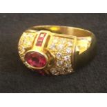 An 18ct gold ruby & diamond dress ring, the oval bezel set ruby framed by twin emerald cut rubies in