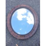 An Edwardian oval mirror with bevelled plate in grained cushion moulded frame.