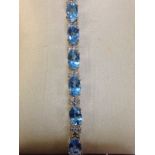 An 18ct gold blue topaz & diamond bracelet, with twenty one claw set blue topaz stones weighing over